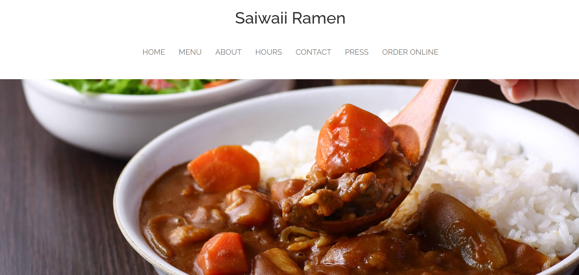 Close-up of a bowl of Japanese curry with chunks of beef, carrots, and potatoes served alongside white rice, with a hand holding a wooden spoon at Saiwaii Ramen.